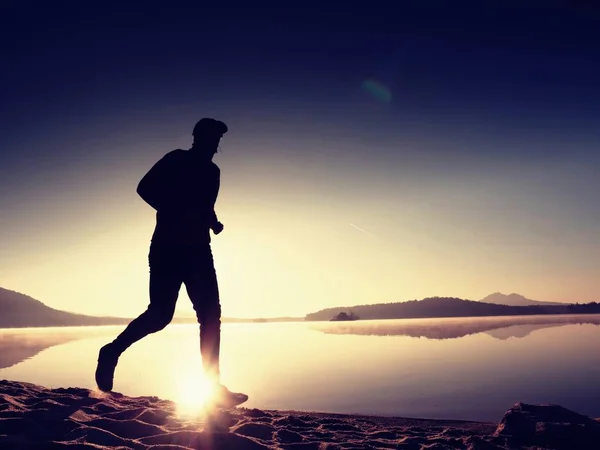 Man running on beach against backdrop of a beautiful sunset. Sand of mountain lake — Stock Photo, Image