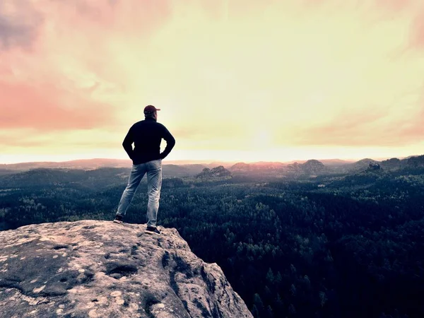 Hiker man stays on a rocky ridge and enjoy view over long valley to horizon. Cold Sun hidden in clouds — Stock Photo, Image