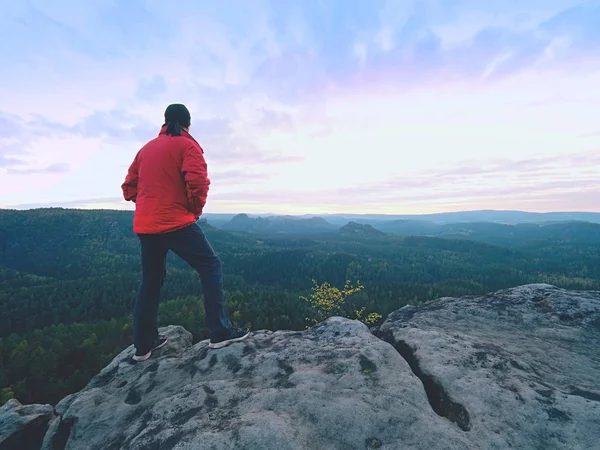 Mann Silhouette auf Klippe. Wanderer in roter Jacke kletterten auf den Gipfel und genossen die Aussicht. Mann wacht über Tal — Stockfoto