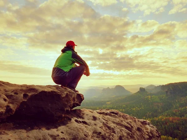 Один турист отдыхает. Турист в зеленой черной куртке, сидящий на скалистой вершине — стоковое фото
