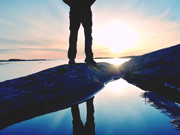 背の高いハイカーのバックパックと暗いスポーツ ウエアでは、海の上の崖に立っています。男は、すばらしい夕日をお楽しみください。 — ストック写真