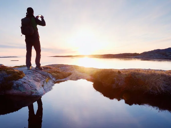 Silueta trasera del viajero tomando selfie en el mar. Turista con mochila de pie sobre una roca — Foto de Stock