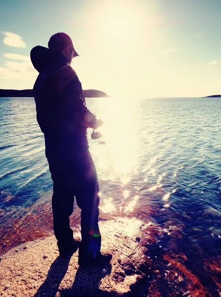 La silhouette di un pescatore che lancia spinning all'alba. L'uomo attivo sta pescando in mare — Foto Stock