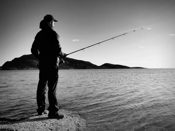 Rybář zkontrolovat rybaření linky a tlačí návnada na tyči, připravit se a hodit návnadu daleko do klidné vody. — Stock fotografie