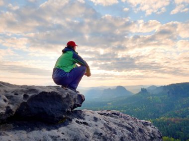 Yeşil siyah ceketli muhteşem görünümü f tadını çıkarırken kayalık tepe üzerinde oturan yetişkin turist görünümünü arka