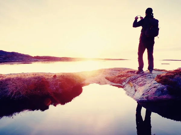 Silhouette posteriore dell'uomo viaggiatore che si fa selfie in mare. Turista con zaino in piedi su una roccia — Foto Stock