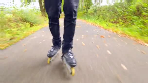 Patinage à roues alignées en plein air sur asphalte glissant humide dans la forêt automnale. Jambes d'homme en pantalon de course noir. Mouvement rapide des bottes en ligne sur la route couverte de feuilles automnales colorées .. — Video