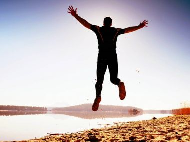 Kumsalda atlama deli adam. Kumsalda güneşin ufuk yukarıda sırasında uçan sporcu