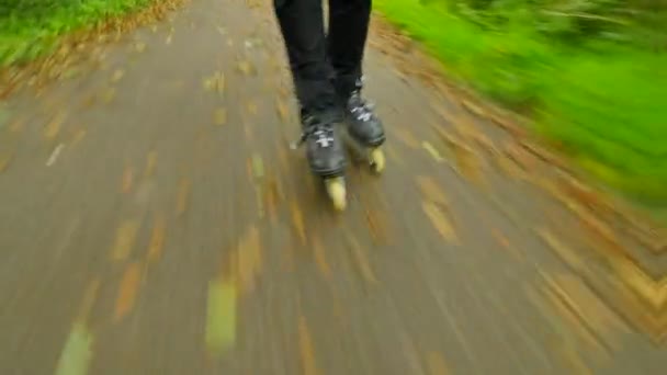 Patinaje en línea al aire libre sobre asfalto húmedo y resbaladizo en bosque otoñal. Piernas de hombre en pantalones negros. Movimiento rápido de las botas en línea en el camino cubierto con hojas de colores otoñales .. — Vídeo de stock