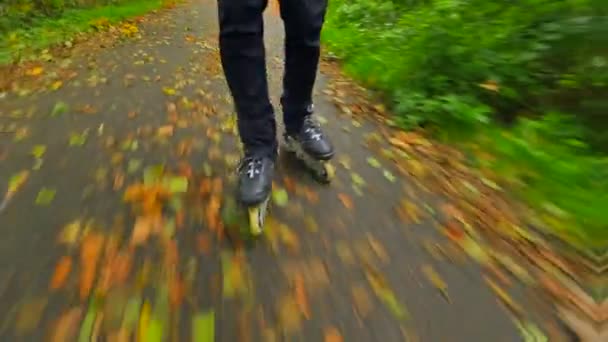 Patinaje en línea al aire libre sobre asfalto húmedo y resbaladizo en bosque otoñal. Piernas de hombre en pantalones negros. Movimiento rápido de las botas en línea en el camino cubierto con hojas de colores otoñales .. — Vídeo de stock