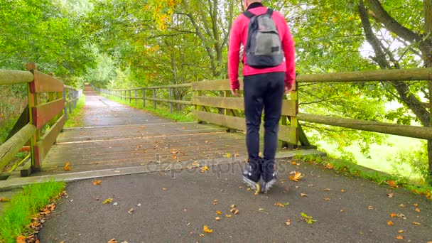 Utomhus inlines. Sportsman i rosa och svart sportkläder med svart rullskridskor och svart ryggsäck. Mannen är snabbt blading på våt asfalt väg i park, färgglada löv på marken — Stockvideo