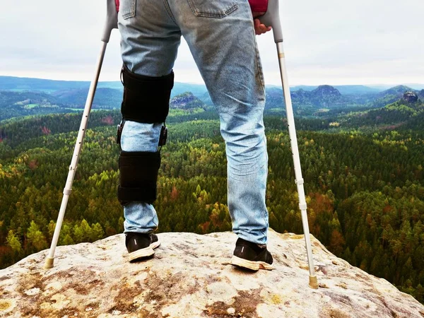 Man Walking With Crutches  in nature. Man legs in jeans with adjustable Bandage on pain knee.
