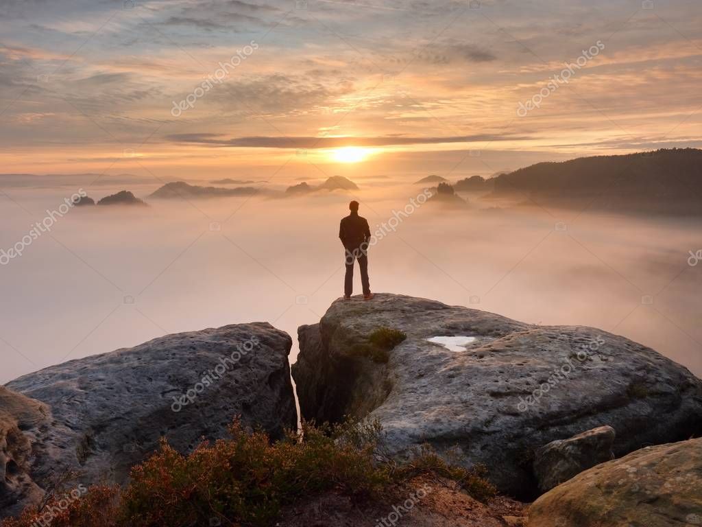 Man stands alone on the peak of rock. Hiker watching to autumn Sun at