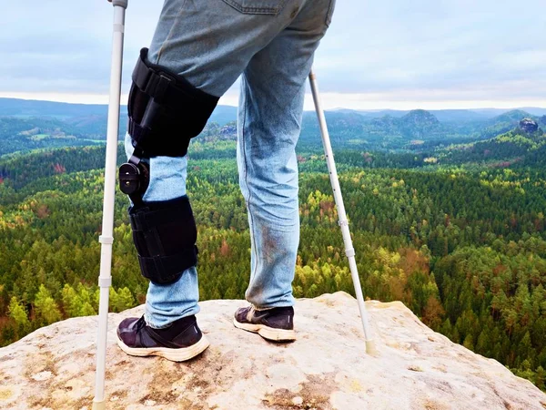 Adam yürüme ile koltuk değneği doğada. Adam bacaklarda ağrı diz ayarlanabilir bandaj ile kot. — Stok fotoğraf