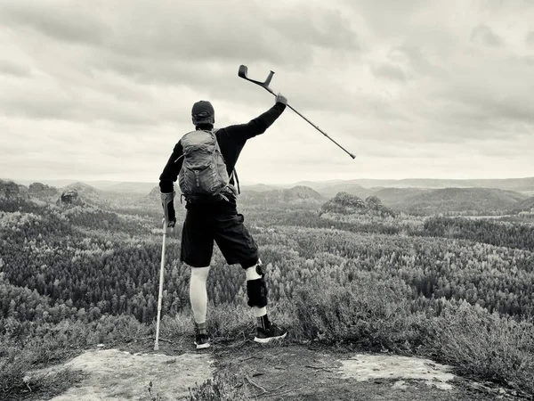 Disabled man on crutches on rock. Hurt knee in neoprene metal knee braces and man hold forearms crutches.
