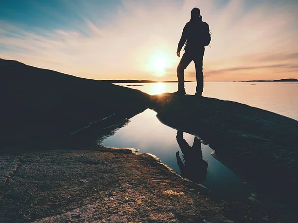 Senderista alto en ropa deportiva oscura con mochila se encuentra en el acantilado sobre el mar. Hombre disfrutar increíble puesta de sol — Foto de Stock