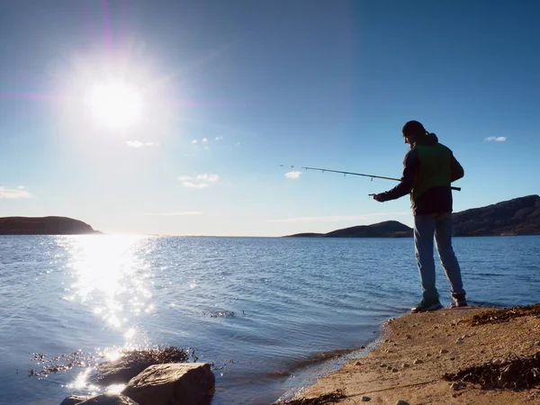 Pescatore controllare la lenza e spingendo esca sulla canna, prepararsi e gettare esca lontano in acqua pacifica . — Foto Stock