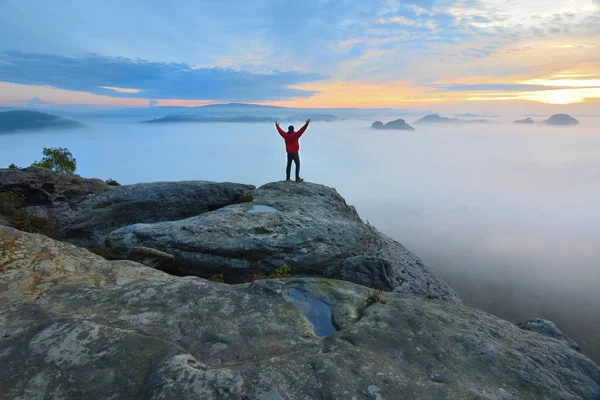 Escursionista su roccia fine sopra valle. L'uomo veglia sulla nebbiosa e autunnale valle del mattino al sole del mattino luminoso . — Foto Stock