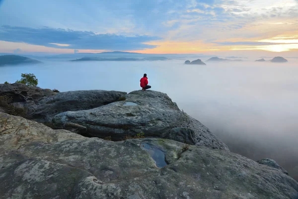 Escursionista su roccia fine sopra valle. L'uomo veglia sulla nebbiosa e autunnale valle del mattino al sole del mattino luminoso . — Foto Stock