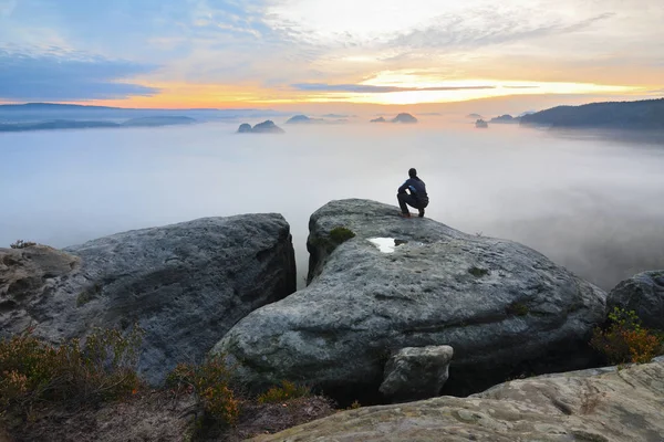 Uzun yürüyüşe çıkan kimse rock ve renkli sis ve sis sabah Vadisi'nde izlerken tepe üzerinde çömelme pozisyonda.
