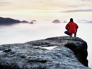 Siyah pantolon, ceket ve karanlık kap yetişkin turist oturup Cliff'in kenar ve puslu tepelik Vadisi'ne bakıyor