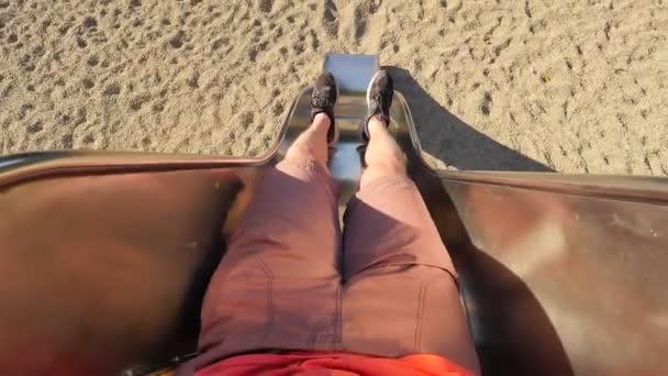 Roll down on chrome steel slider on playground. Legs with running shoes make movement to start sliding and than slide down into sandy ground. The first person view — Stock Video