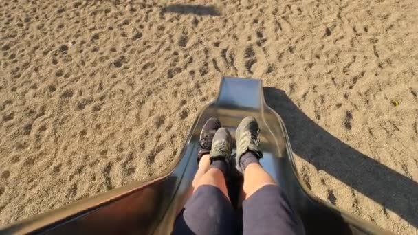 Roll down on chrome steel slider on playground. Man and children legs  make movement to start sliding and than slide down into sandy ground. The first person view — Stock Video