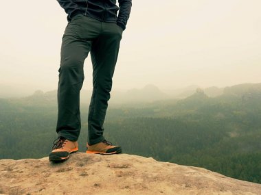 Karanlık yürüyüş pantolon ve kaya sisli vadinin üstünde tepe üzerinde deri trekking ayakkabı erkek bacaklarda. Anahat Hill 