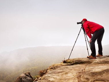 Uzun yürüyüşe çıkan kimse ile fotoğraf makinesi tripod üzerinde kayalık Zirvesi resimden alır. Yalnız fotoğrafçı Zirvesi