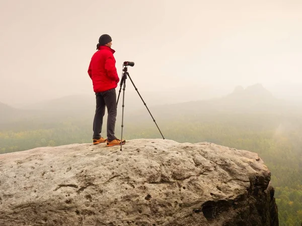 Fotógrafo pensar sobre a imagem no pico nas montanhas nebulosas. Vale escondido em névoa pesada — Fotografia de Stock