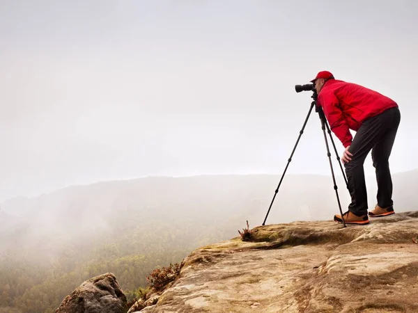 Escursionista con macchina fotografica su treppiede scatta foto dalla cima rocciosa. Fotografo da solo in vetta — Foto Stock