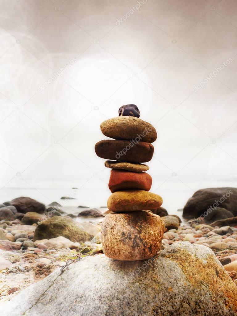 Balanced stone pyramid on sea shore, waves in background. Colorful stones 