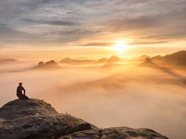 Turista sedersi sulla cima di roccia arenaria e guardare in nebbia colorata e nebbia nella valle del mattino. Triste uomo — Foto Stock