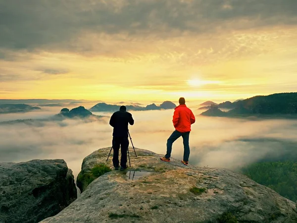 Fotograf med øye for kamerafunneren på tripod... Hold deg på klippen og ta bilder, snakke med venner... . – stockfoto