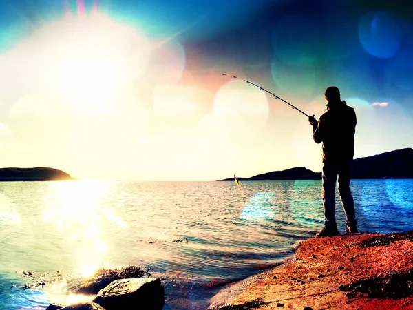 Der aktive Mann fischt auf See von der Felsküste aus. Fischer überprüfen, ob Köder auf der Angelschnur liegen — Stockfoto