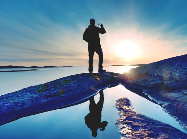 Silhouette arrière d'un voyageur prenant un selfie en mer. Touriste avec sac à dos debout sur un rocher — Photo