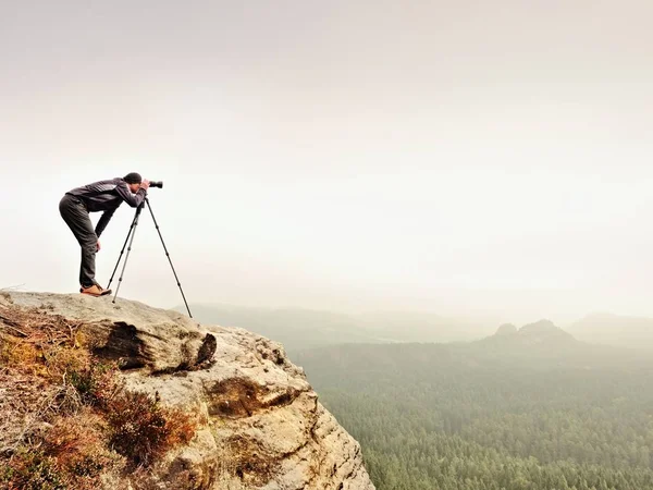 Caminhante com câmera no tripé tira foto do cume rochoso. Fotógrafo sozinho na cimeira — Fotografia de Stock