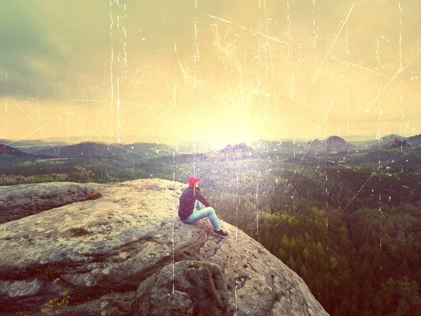 Caminante en Cliff. Turista en gorra roja, sudadera negra y jeans se sientan en un acantilado de montaña sobre el valle —  Fotos de Stock