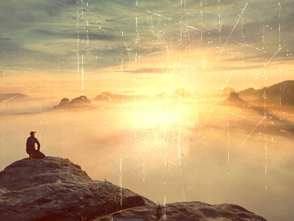 Турист сидит на вершине песчаника и наблюдает за красочным туманом и туманом в утренней долине. Грустный человек. Сядь. Человек в джинсах. Падающий горный туман — стоковое фото