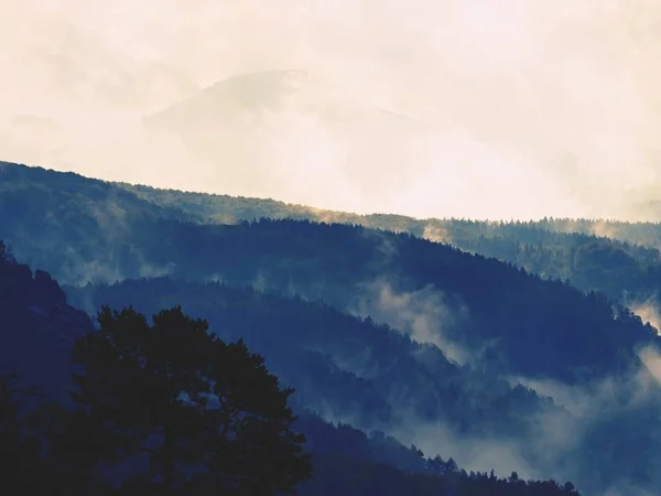 Distant mountain range and heavy clouds of colorful  mist above deep valleys — Stock Photo, Image