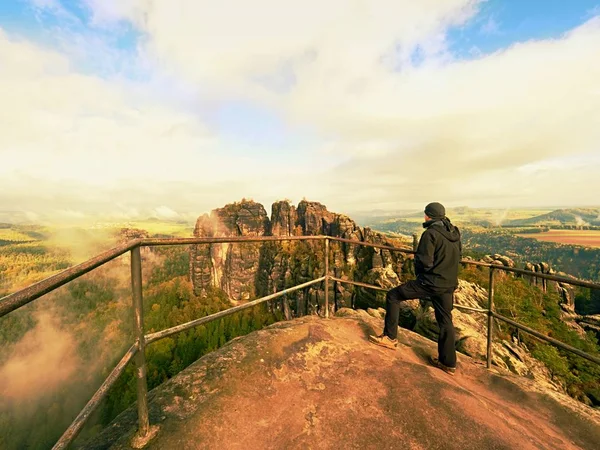 Homem caminhante no corrimão no pico da rocha assistindo em paisagem enevoada — Fotografia de Stock