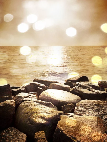 Boulders at island shore stick up from smooth sea. Stony coast defies to waves of ocean