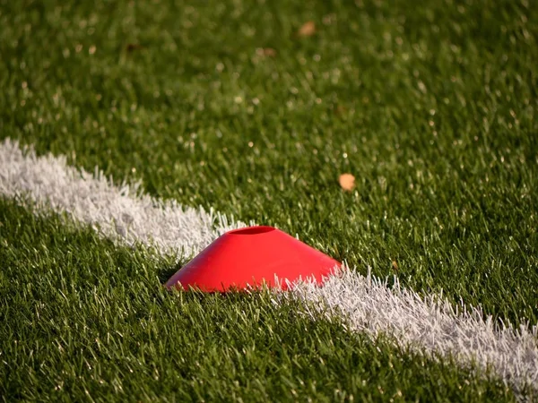 Cono di plastica rosso brillante su linea bianca dipinta di campo di calcio. Plastica calcio verde tappeto erboso — Foto Stock