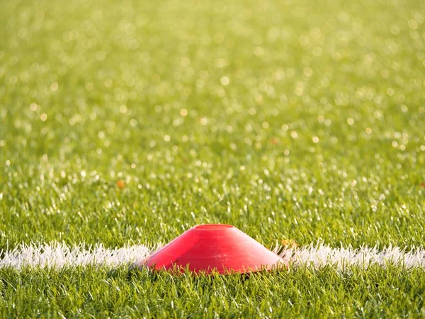 Ярко-красный пластиковый конус на белой линии футбольного поля. Пластиковая футбольная зеленая площадка — стоковое фото
