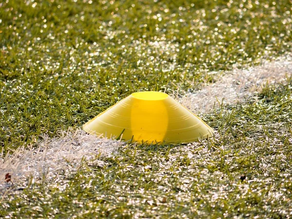 Cono de plástico amarillo brillante en línea blanca. Fútbol de plástico verde césped patio de recreo con moler caucho negro — Foto de Stock