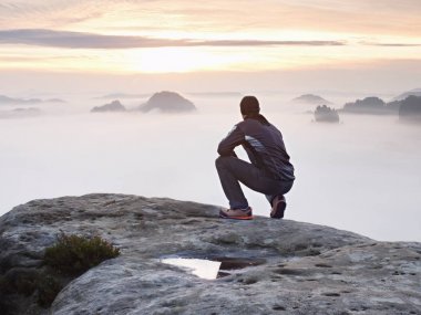 Turistik zirve kumtaşı kaya ve renkli sis ve sis sabah Vadisi'nde izlerken oturmak. Üzgün adam