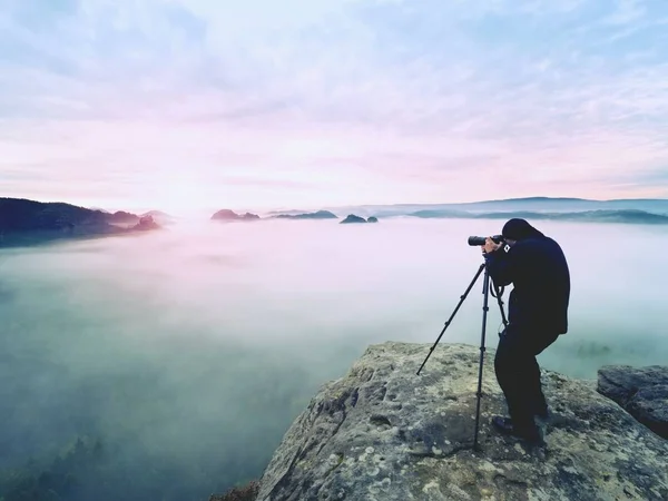 Professional på klippa. Naturfotograf tar bilder med spegel kamera på toppen av rock. Drömmande dimma — Stockfoto