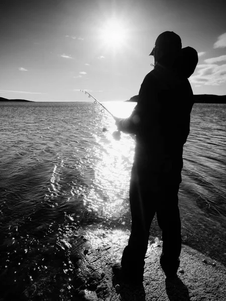 Рибалка перевіряє рибальську лінію і штовхає приманку на стрижень. Силует рибалки на заході сонця — стокове фото