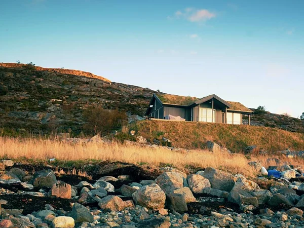Ένα παραδοσιακό ξύλινο κόκκινο σπίτι καμπίνα παρακάτω βραχώδη λόφο. Σπίτι στο κλασικό σχεδιασμό για Νορβηγία — Φωτογραφία Αρχείου