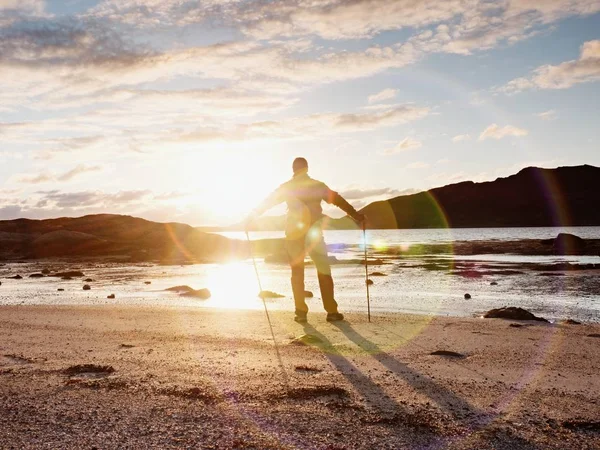 Spaziergänger beobachten den sonnigen Frühlinganbruch über dem Meer. Wanderer mit Rucksack stehen am sandigen Ufer. Sonnenstrahlen — Stockfoto